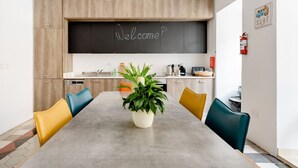 Eine moderne Küche mit einer Kreidetafel, auf der 'Welcome' steht, einem Esstisch mit Stühlen und einem Blumentopf.