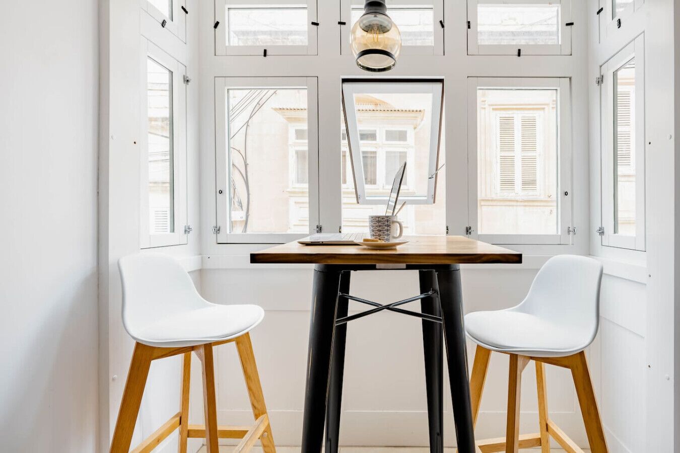 A dining area with a table and two white chairs, a lamp, and a view through the windows.