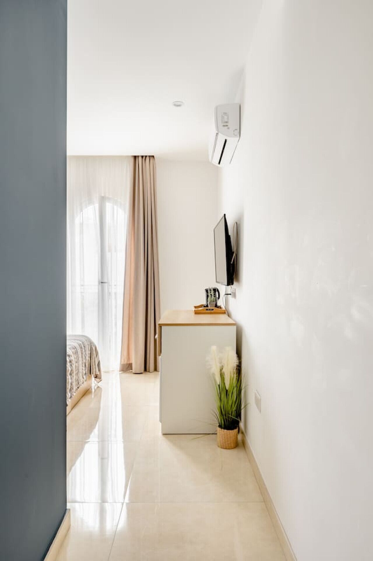 Moderni hotellihuone, jossa on sänky, pieni työpöytä, televisio ja ruukussa oleva kasvi.