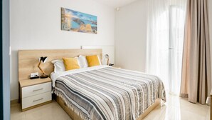 Een slaapkamer met een bed, nachtkastje, lamp, schilderij aan de muur en raam met gordijnen.