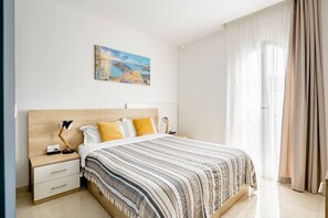 A bedroom with a bed, a nightstand, a lamp, a painting on the wall, and a window with curtains. - MarsaxlokkRoom - Hammock Vibes Towns House (Tas-Sliema)