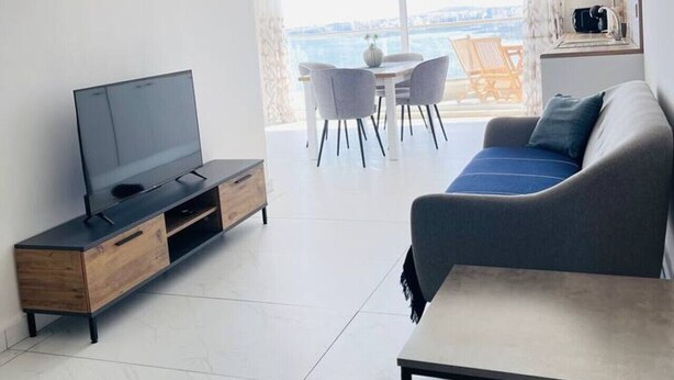 Un soggiorno moderno con televisione a schermo piatto, un divano, un tavolo da pranzo con sedie e un'ampia finestra che offre una vista.