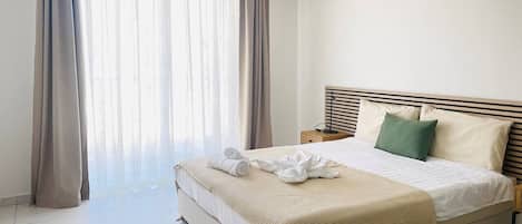 A hotel room with a bed, curtains, an air conditioning unit, and a bedside table.