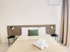 Een hotelkamer met een bed, twee nachtkastjes, een groen kussen en een opgerolde handdoek op het bed.