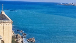 Vista sulla costa con un edificio caratterizzato da una torre imponente e un litorale roccioso.