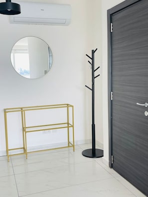 Ein Zimmer mit einer dunkelbraunen Holztür, einem runden Spiegel, einer goldrahmigen Regalwand und einem schwarzen Kleiderständer.