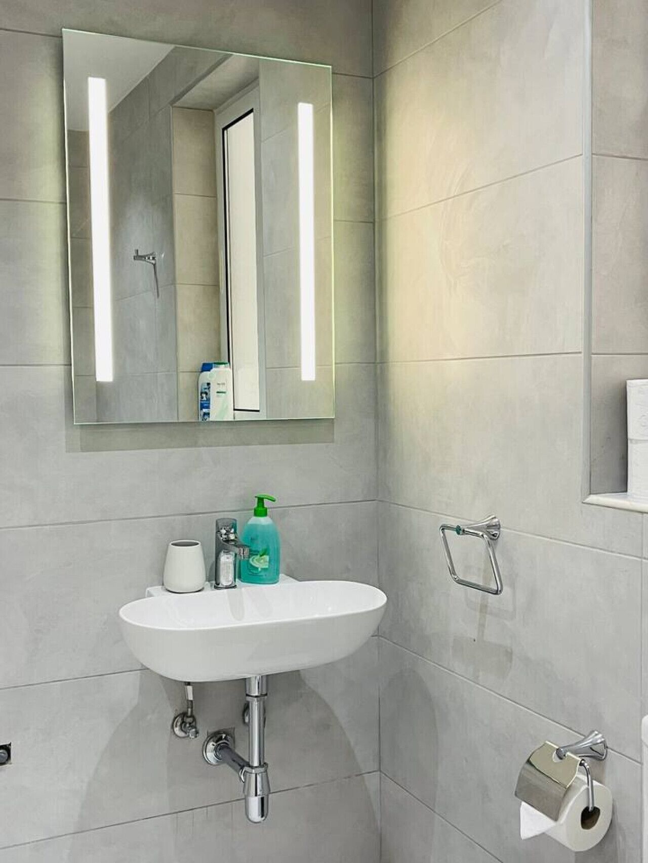 Une salle de bain avec un lavabo blanc, un miroir et un porte-serviettes.