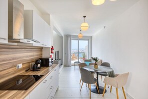 A modern kitchen with a wooden countertop, a dining area with a round table and chairs, and a view of the city through large windows.