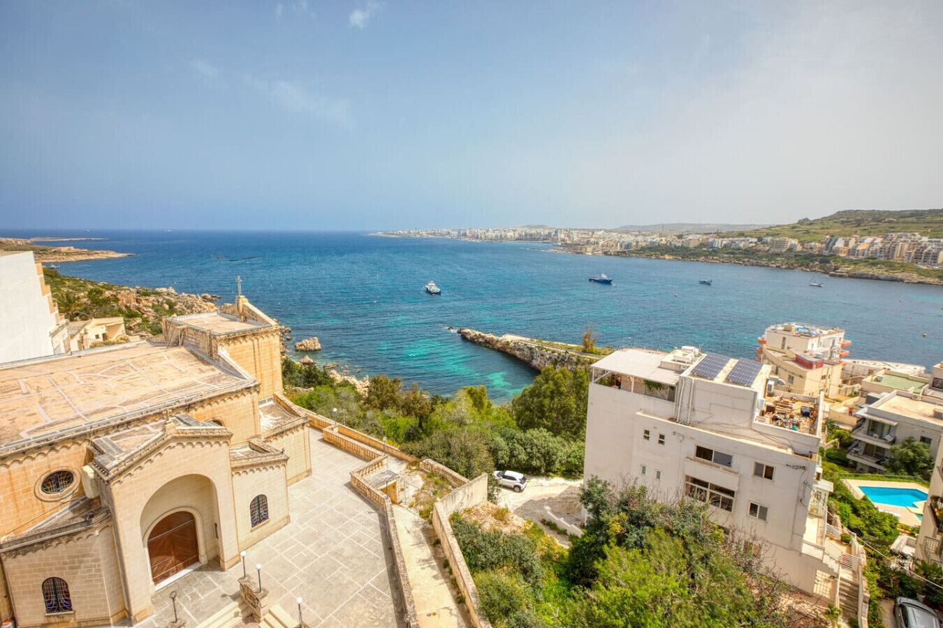 A coastal cityscape with a historic building, a modern apartment complex, and a clear view of the sea.