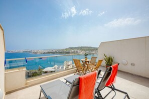 A balcony with a view of the sea, a table, chairs, and a potted plant.