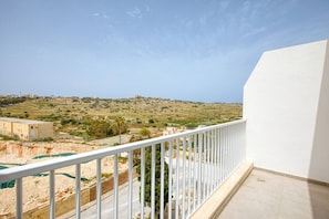 A balcony with a white railing overlooking a hilly landscape with buildings and greenery.