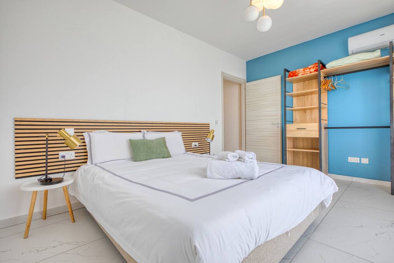 Une chambre d’hôtel moderne avec un grand lit, des tables de chevet, une armoire et un mur d’accent bleu.