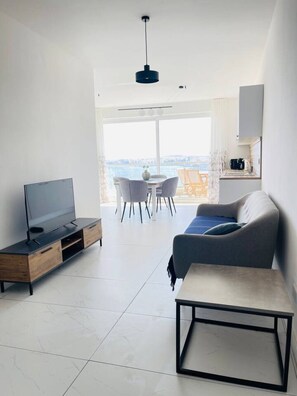 A modern living room with a flat-screen TV, a sofa, a coffee table, and a dining area with chairs. - Blu Mar Sea View Appartment 4 (San Pawl il-Baħar)