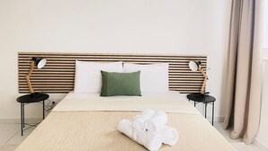 A hotel room with a bed, two bedside tables, a green pillow, a rolled white towel, and an air conditioning unit. - Blu Mar Sea View Appartment 4 (San Pawl il-Baħar)