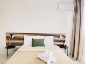 A hotel room with a bed, two bedside tables, a green pillow, a rolled white towel, and an air conditioning unit. - Blu Mar Sea View Appartment 4 (San Pawl il-Baħar)