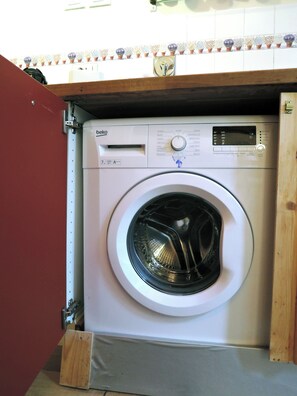 A front-loading washing machine with a control panel, a wooden cabinet above it, and a tiled backsplash with a floral pattern. - Bright Romantic Retreat in Florence (Firenze)
