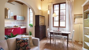 A cozy living room with a sofa, a dining table with chairs, a kitchen area with a red cabinet, and a large window with curtains. - Bright Romantic Retreat in Florence (Firenze)
