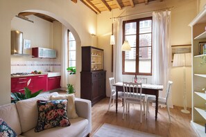 A cozy living room with a sofa, a dining table with chairs, a kitchen area with a red cabinet, and a large window with curtains. - Bright Romantic Retreat in Florence (Firenze)