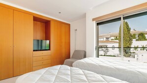 Ein Schlafzimmer mit zwei Betten, einem Holzschrank, einem Fernseher und einem großen Fenster mit Blick auf Gebäude.