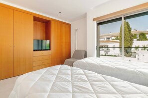 A bedroom with two beds, a wooden wardrobe, a television, and a large window with a view of buildings. - Charming Holiday House With Stunning Views in Albufeira (Albufeira)
