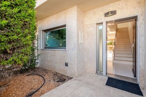A modern building entrance with a glass door, a window, and a small outdoor area with gravel and a hose. - Charming Holiday House With Stunning Views in Albufeira (Albufeira)