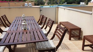 Eine Außenpatio mit Holztisch und -stühlen, einem Pool im Hintergrund und Blick auf die umliegende Landschaft.
