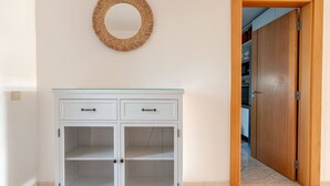 Ein weißes Schränkchen mit zwei Schubladen und zwei Glastüren, einer Holztür und einer gewebten Wanddekoration.