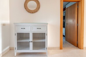 A white cabinet with two drawers and two glass-fronted shelves, a wooden door, and a woven wall decoration. - Charming Holiday House With Stunning Views in Albufeira (Albufeira)