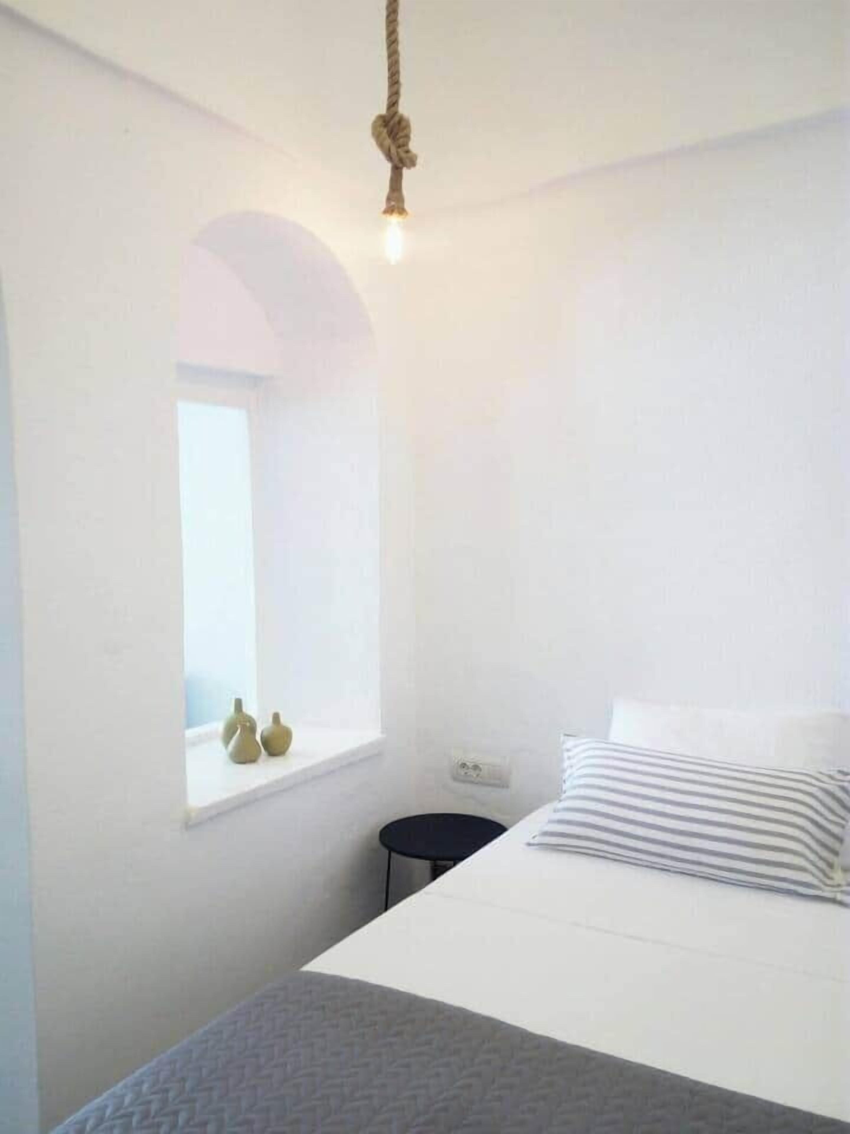 Quarto minimalista com cama, janela e luminária pendente.