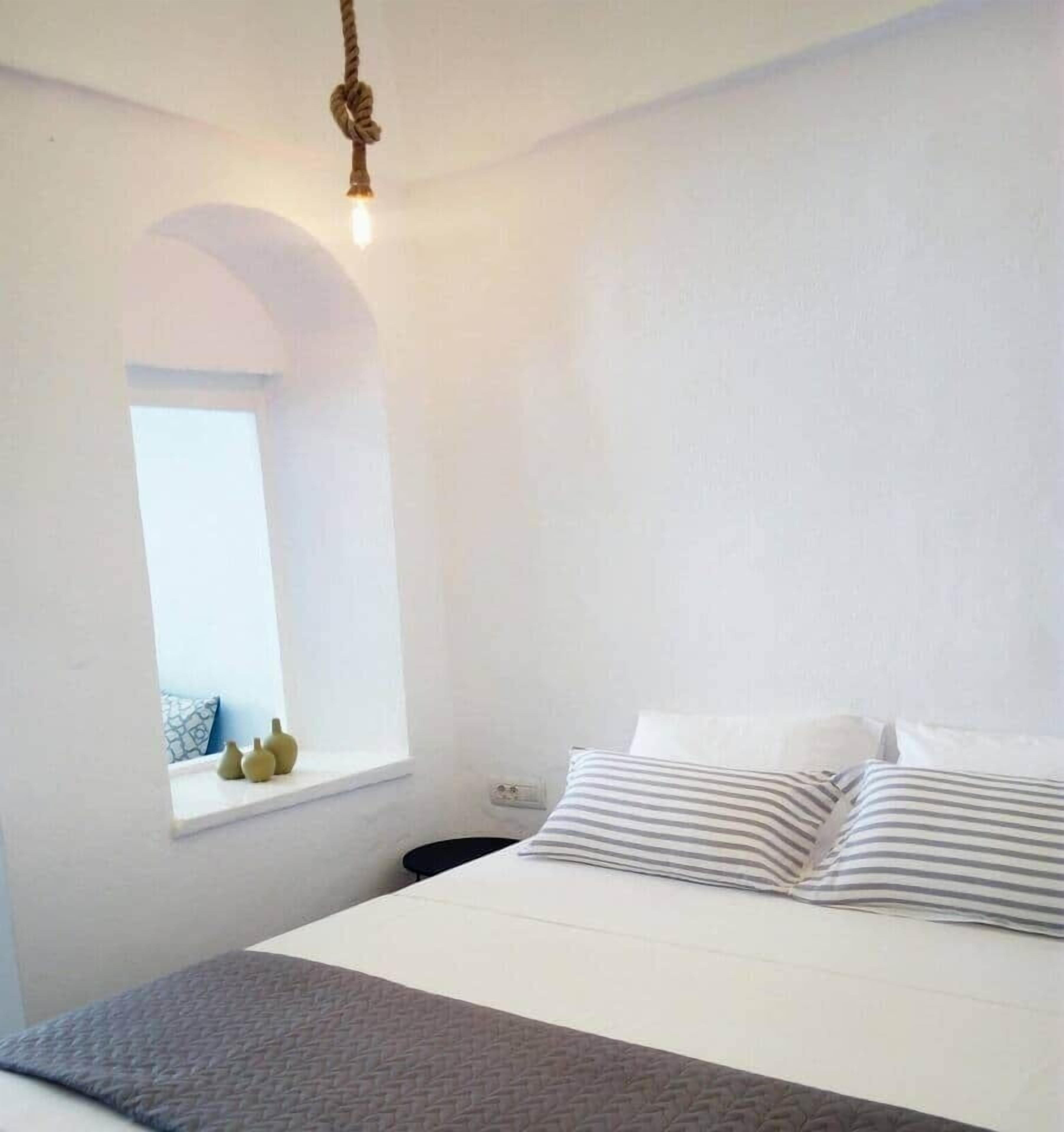 A bedroom with a bed, a window, and a hanging light fixture.