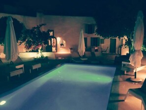 A nighttime swimming pool area with lounge chairs and umbrellas. - Villa LuxL Family House (Mesaria)
