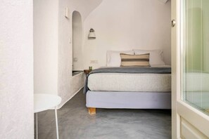 Ein schmales Zimmer mit einem Bett, einem kleinen Tisch und einer Wandlampe.