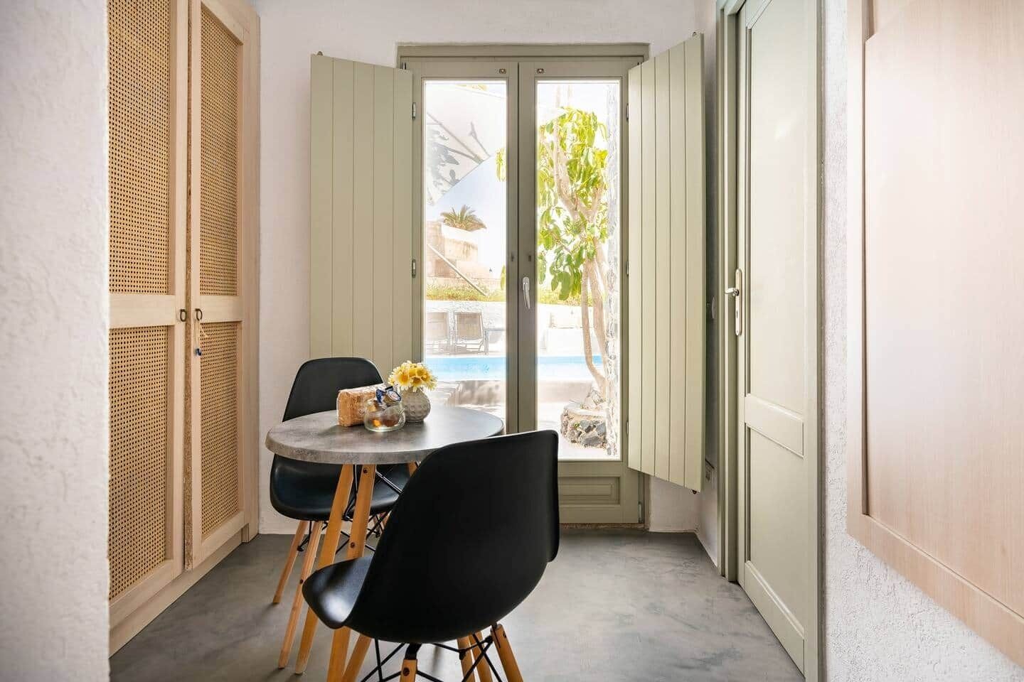 Una habitación pequeña con una mesa y sillas, una puerta que da al exterior y vista a una piscina.