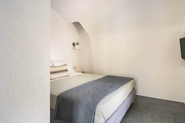A small, narrow room with a bed, a wall-mounted light, and a television. - Villa LuxL Distillery Studio (Mesaria)
