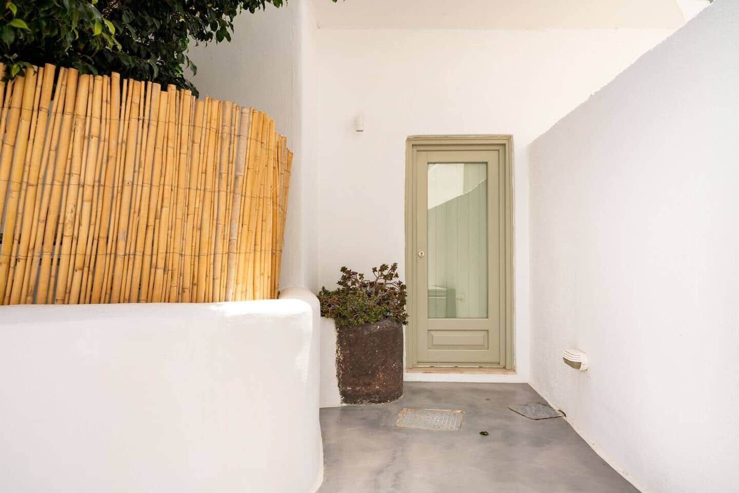 Un petit espace extérieur, délimité par une clôture en bambou, avec une porte et un pot de fleurs.
