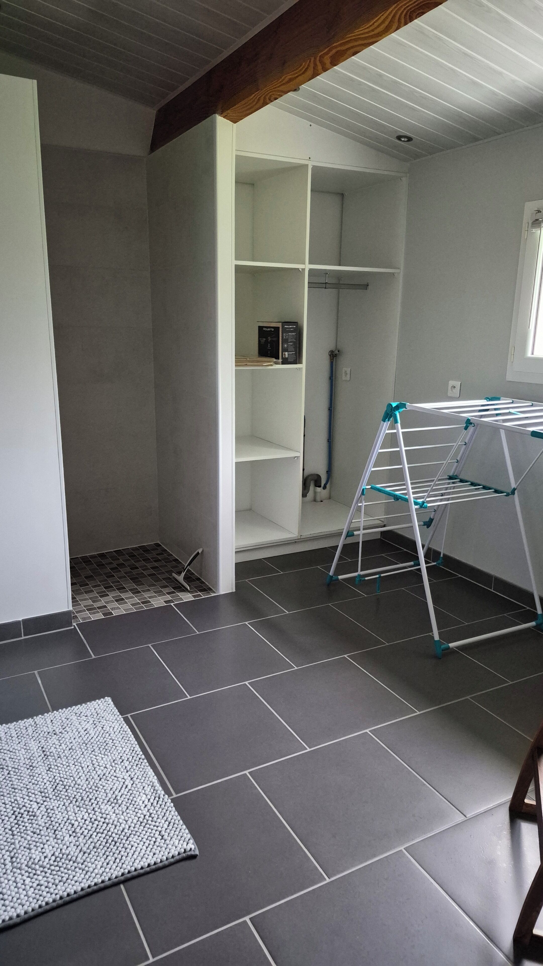 A room with a grey tiled floor, a white wardrobe with open doors, and a drying rack.