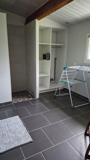 Une pièce avec un sol carrelé de couleur grise, une armoire blanche dont les portes sont ouvertes et un étendoir à linge.
