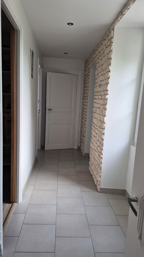 A hallway with a tiled floor, a white door, and a stone wall. - Maison élégante et calme (VOUZAN)