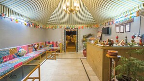 A room with a striped ceiling, a sofa with a colorful quilt, a wooden table, and a reception desk with various items.