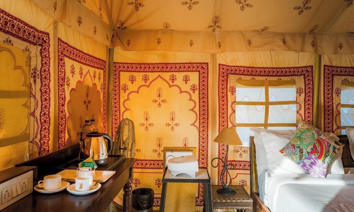 A room with a bed, bedside table, lamp, and a window with curtains.