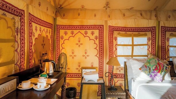 A room with a bed, bedside table, lamp, and a window with curtains.