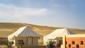 Two white tents with a flat roof, set against a desert landscape with sand dunes in the background.