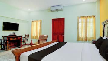A hotel room with a bed, a desk, a chair, a television, and a red door.