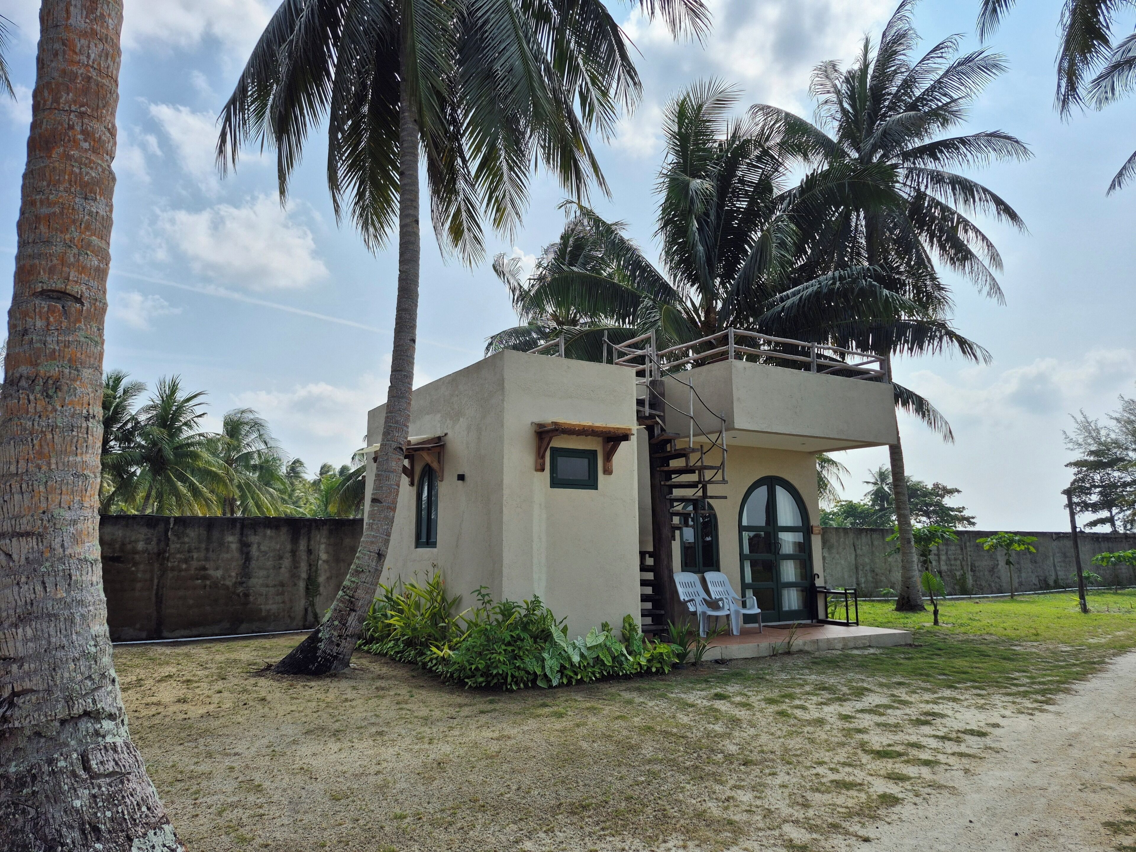 A small, single-story building with a flat roof, surrounded by palm trees and a grassy area.