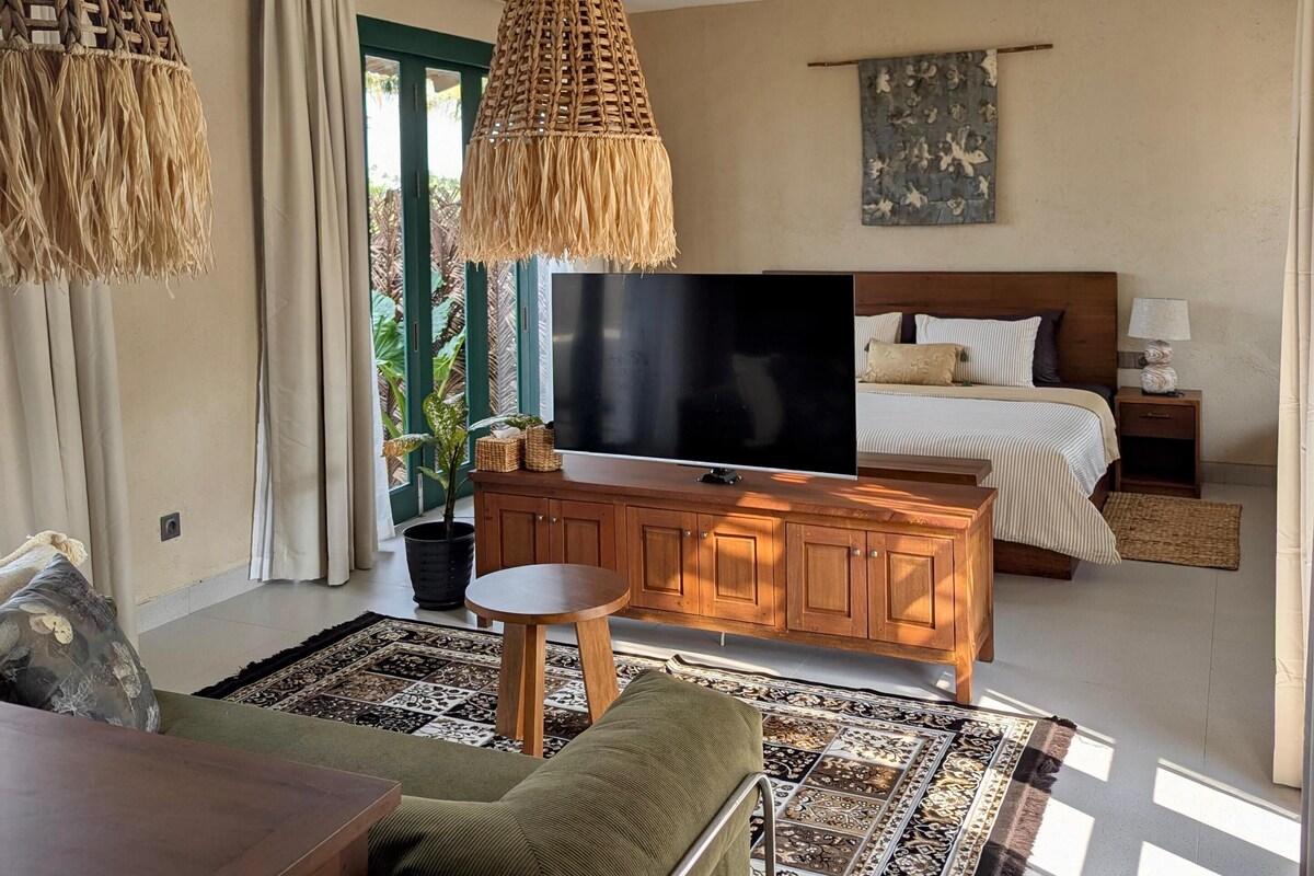 A bedroom with a bed, a TV, a ceiling fan, and a large window.