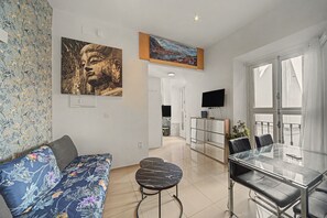 Een moderne woonruimte met een bank, een eettafel met stoelen, een flatscreen-televisie en kunstwerken aan de muren.