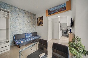 A living room with a sofa, a coffee table, and a TV. There is a kitchen area with a washing machine and a sink. - Central Seville Apartment with Terrace, Balconies, and Prime Location (Seville)
