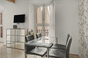 A modern room with a glass table and chairs, a flat-screen TV mounted on the wall, and a window with curtains. - Central Seville Apartment with Terrace, Balconies, and Prime Location (Seville)