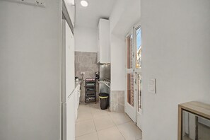 A narrow kitchen with white cabinets, a stainless steel sink, and a tiled floor. - Central Seville Apartment with Terrace, Balconies, and Prime Location (Seville)