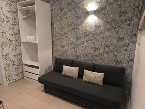 Ein Zimmer mit einer dunklen Couch, gemustertem Wandpapier und einem weißen Kleiderschrank.